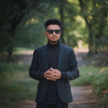 Stylish man in sunglasses and suit standing in a Sylhet forest path during the day.