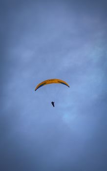 A lone paraglider gracefully flies beneath an overcast sky, capturing a sense of adventure and freedom.