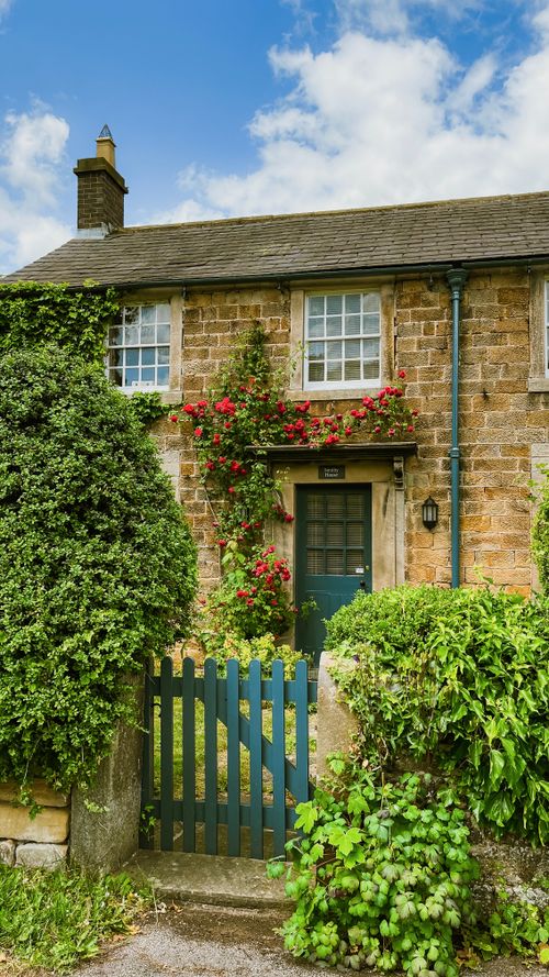 Free Rustic cottage exterior adorned with ivy and flowers, featuring a blue gate and stone facade. Stock Photo