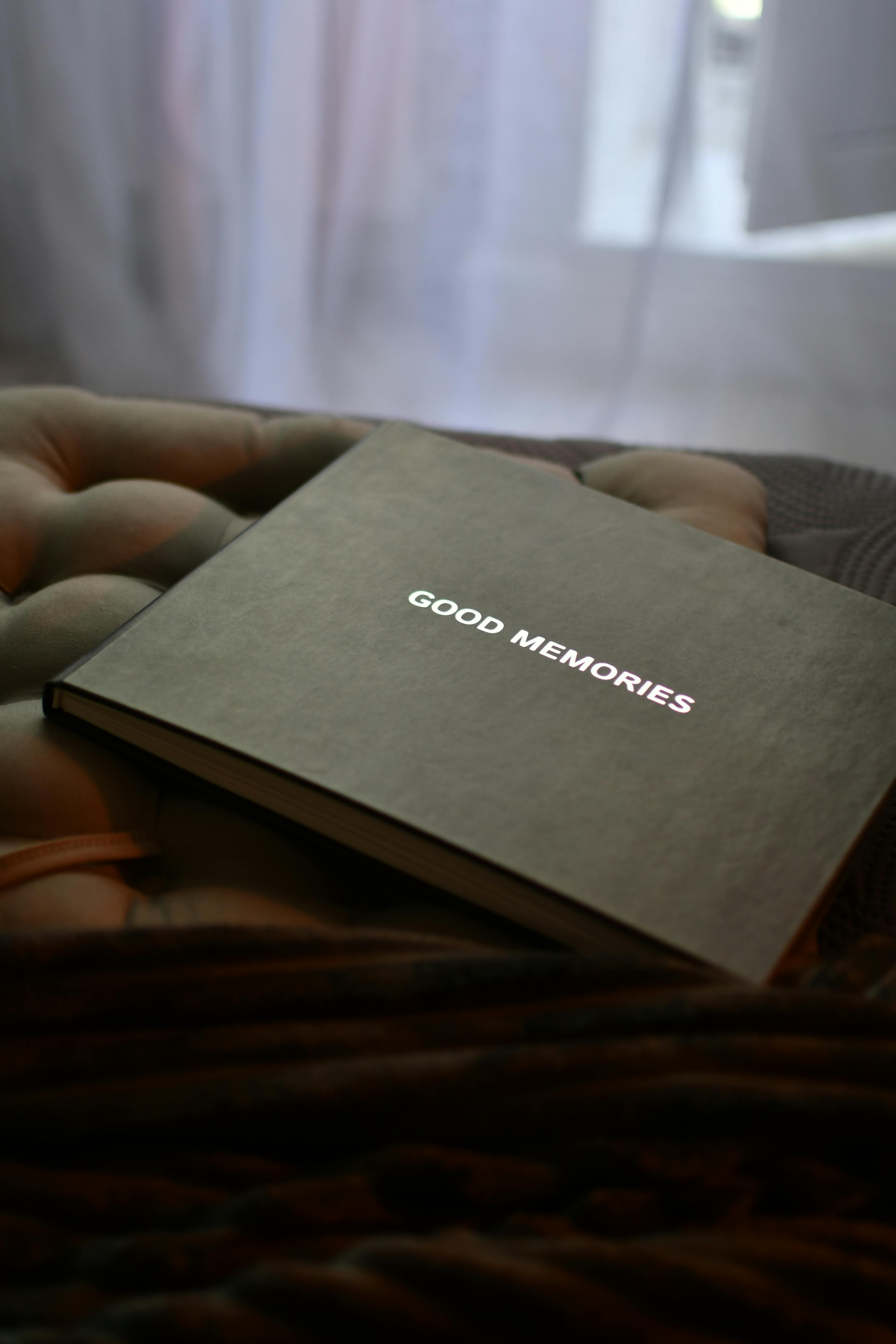 Free Close-up of a photo album titled 'Good Memories' resting on a cozy bed with soft lighting. Stock Photo