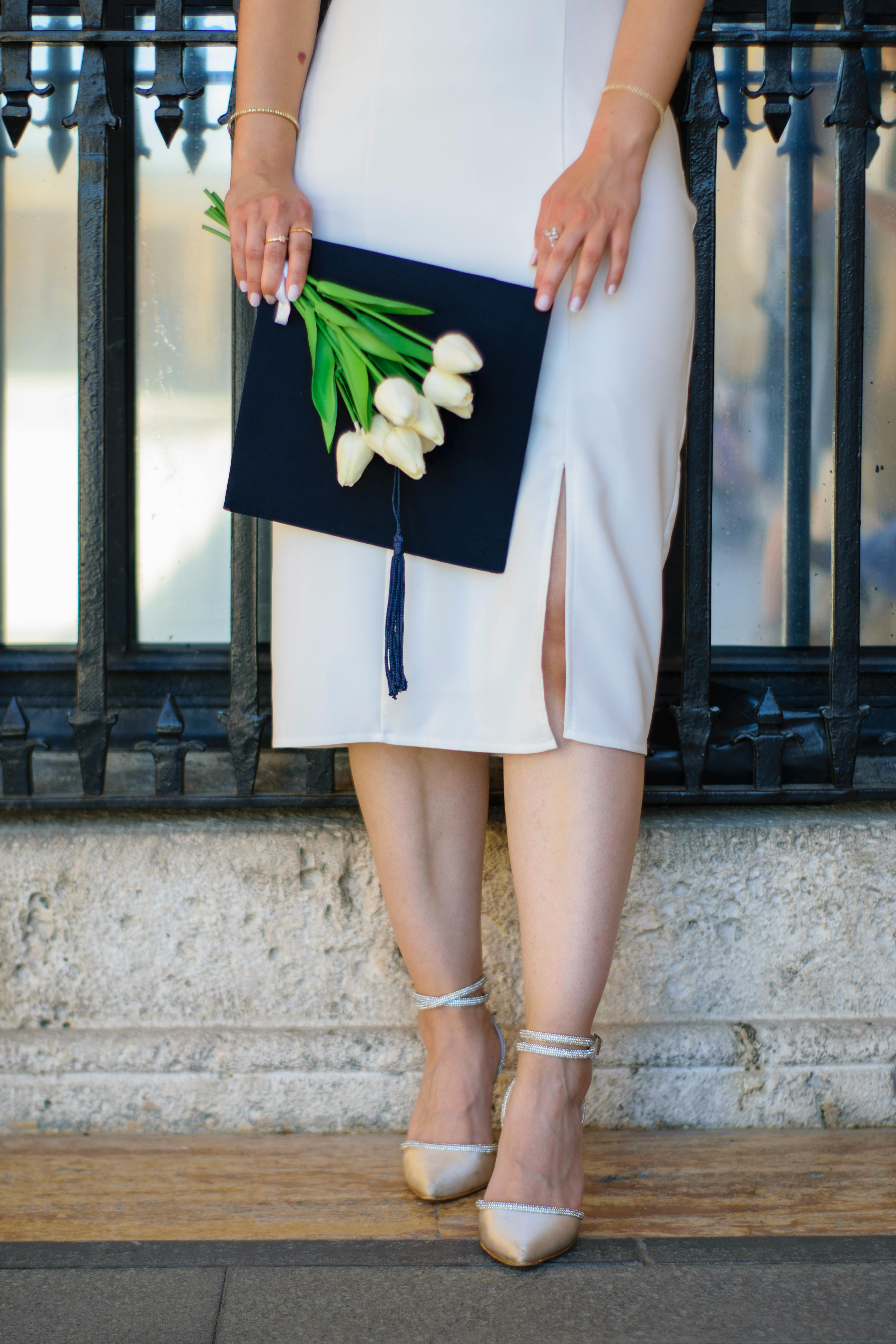 woman in a white dress with a bouquet of white tulips and a graduation hat in her hand