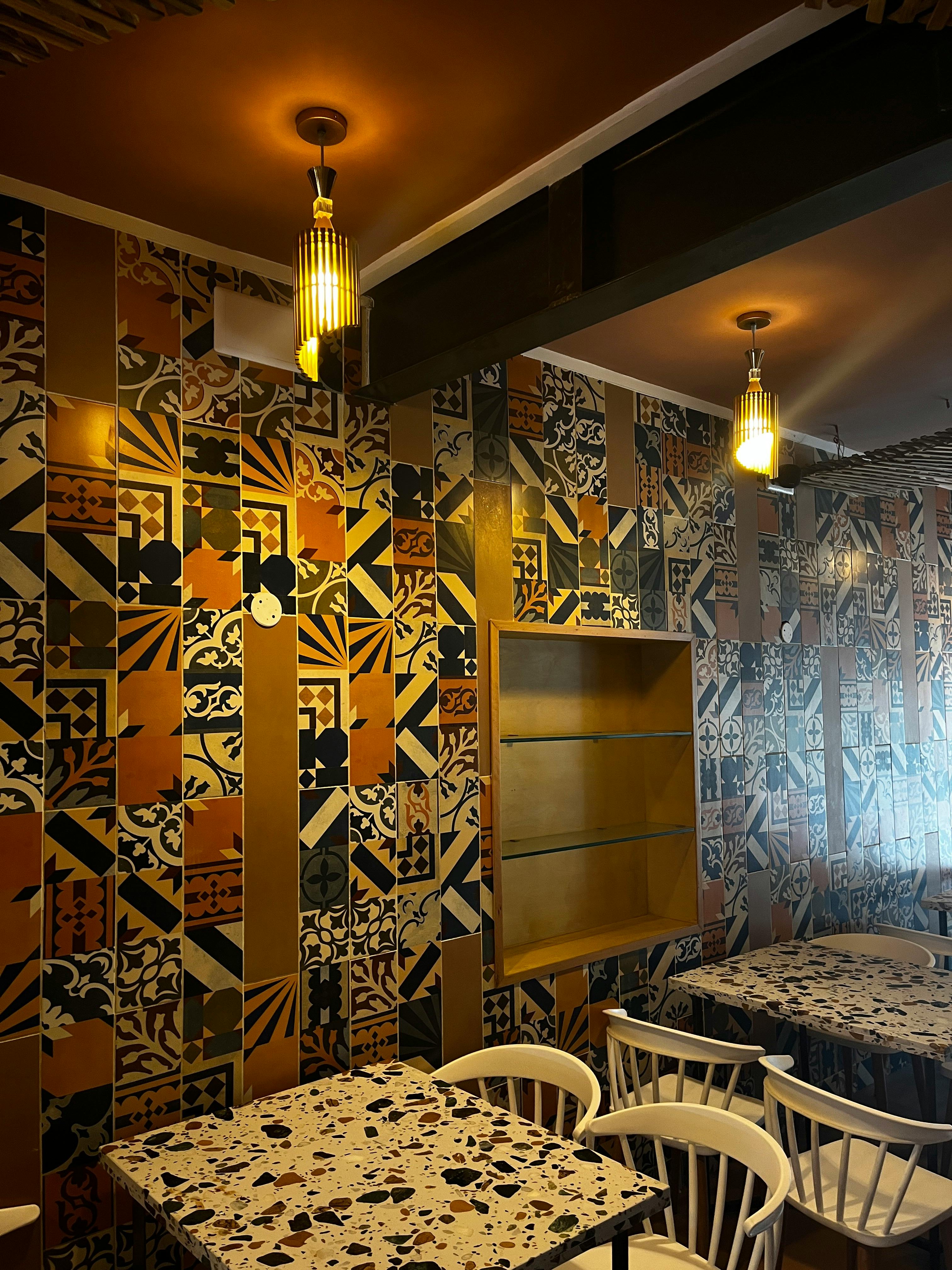 A colorful mosaic-tiled wall in a stylish restaurant with ambient lighting and neat seating arrangement.