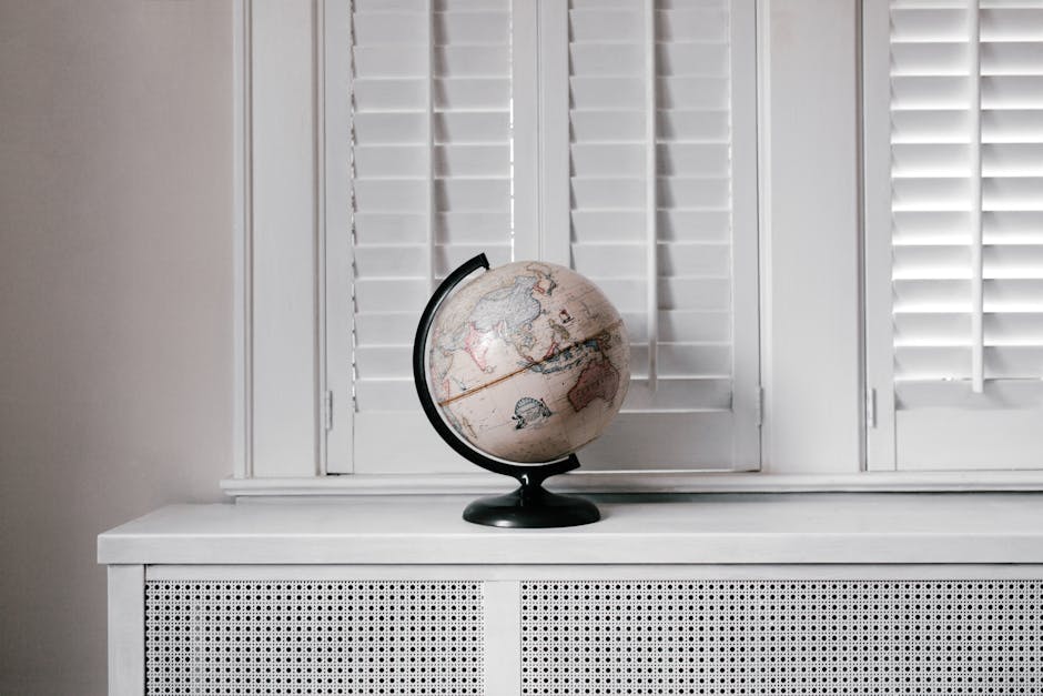 Elegant globe on a minimalist white desk against shuttered windows in modern interior design.
