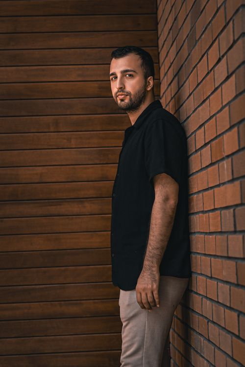 Free Portrait of a man in casual attire leaning against a wooden and brick wall. Stock Photo