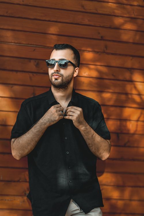 Free A fashionable man poses in sunglasses against a wooden wall, showcasing modern style. Stock Photo