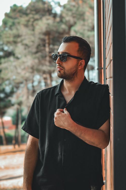 Free Chic man in sunglasses poses casually against a wall, exuding cool style. Stock Photo