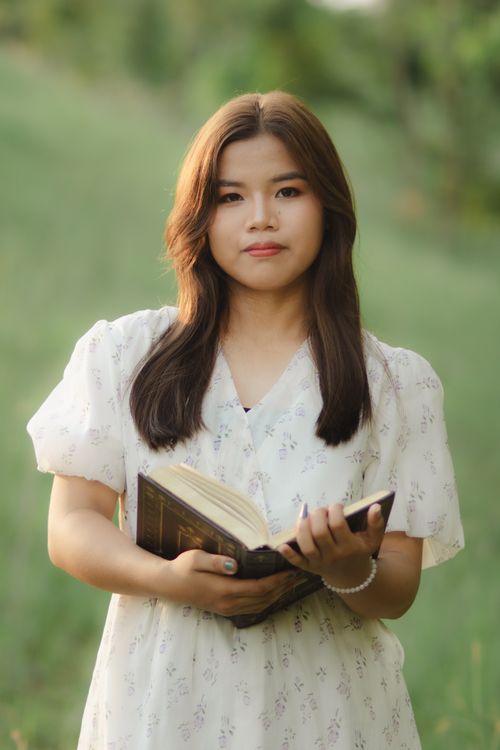 Free Portrait of a woman holding a book in a summer field, wearing a white dress. Stock Photo