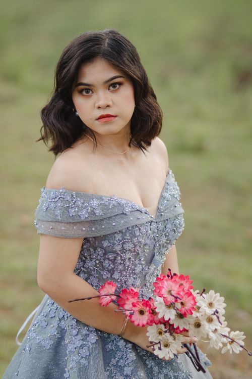 Free Portrait of a woman in a sparkling gown holding flowers in a field in the Philippines. Stock Photo