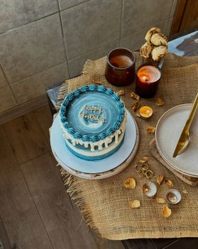 A stylish blue birthday cake with lit candles on a rustic table setting, perfect for party inspiration.