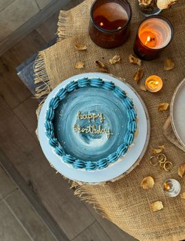 Artistic blue birthday cake with candles on rustic table setting.