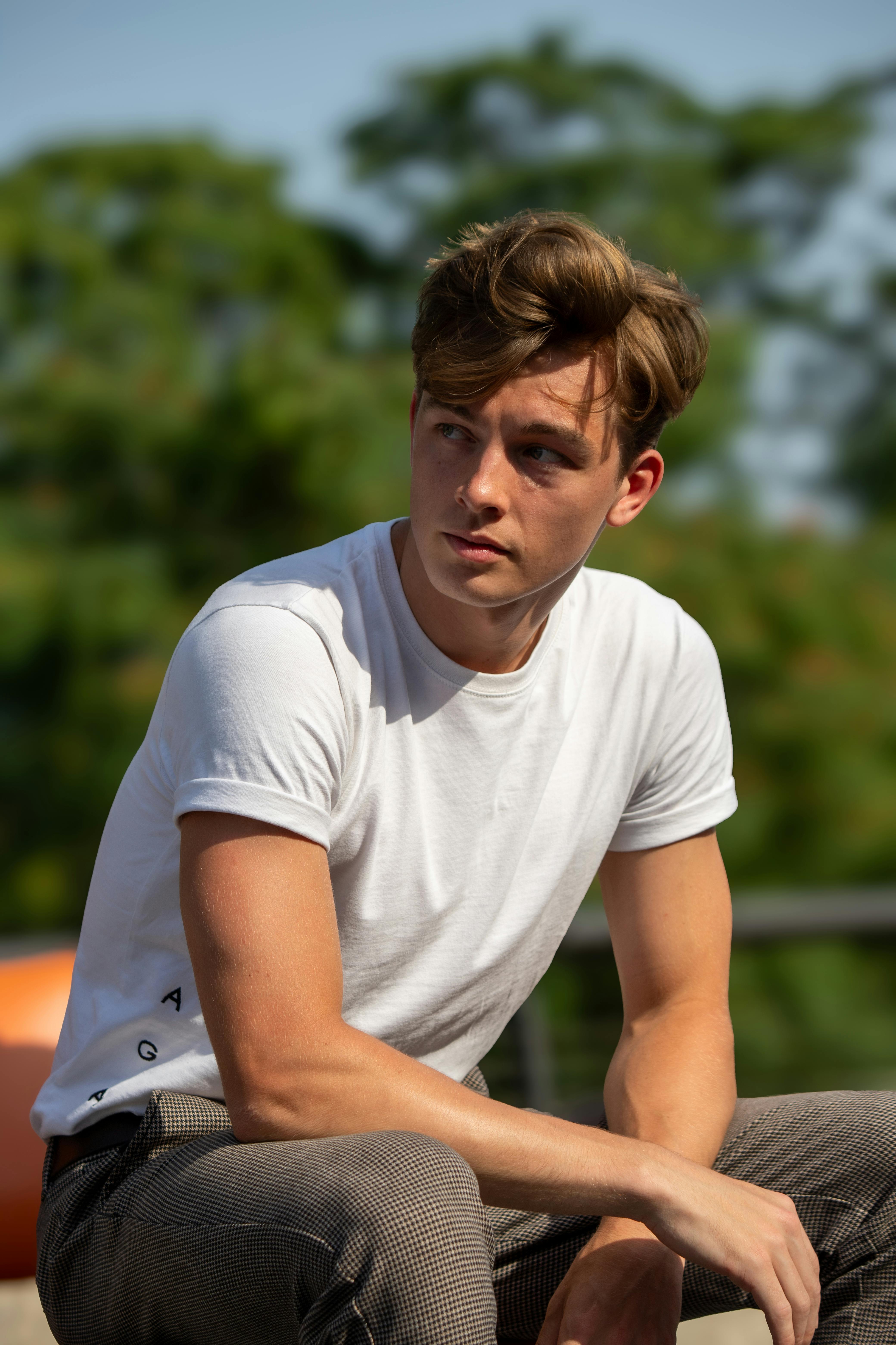 A stylish young man sits outdoors in Berlin, captured in warm summer sunlight.