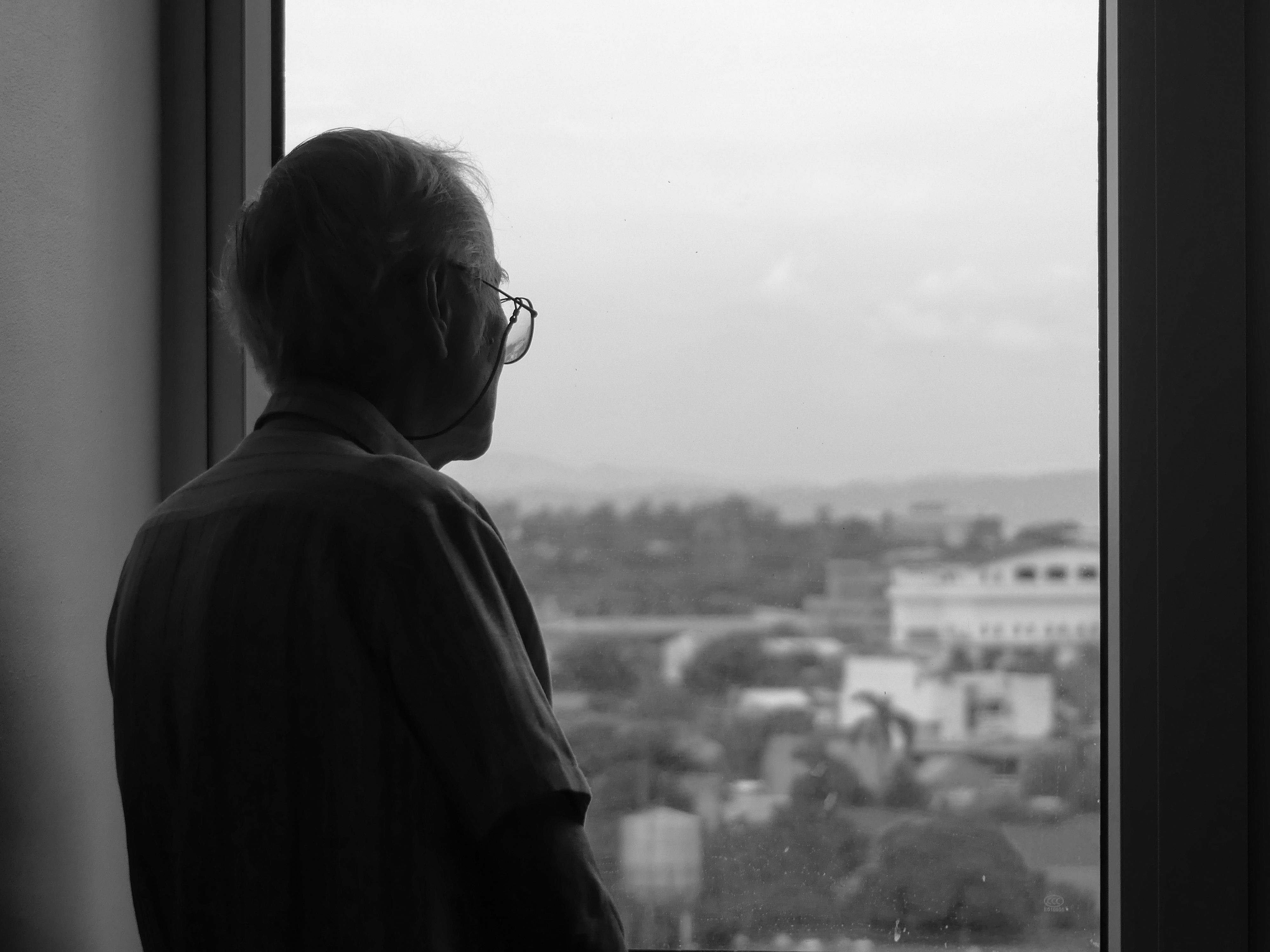 An elderly man in glasses looking through a window in contemplation — the Stanford ibogaine PTSD study enrolled special operations veterans who had already exhausted conventional treatment options