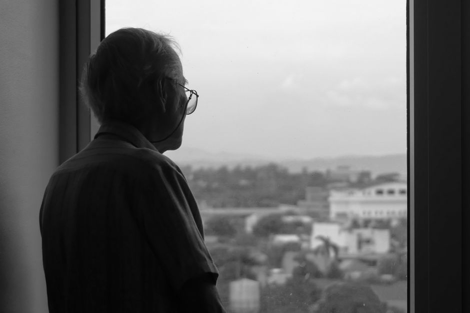 An elderly man in glasses looking through a window in contemplation — the Stanford ibogaine PTSD study enrolled special operations veterans who had already exhausted conventional treatment options