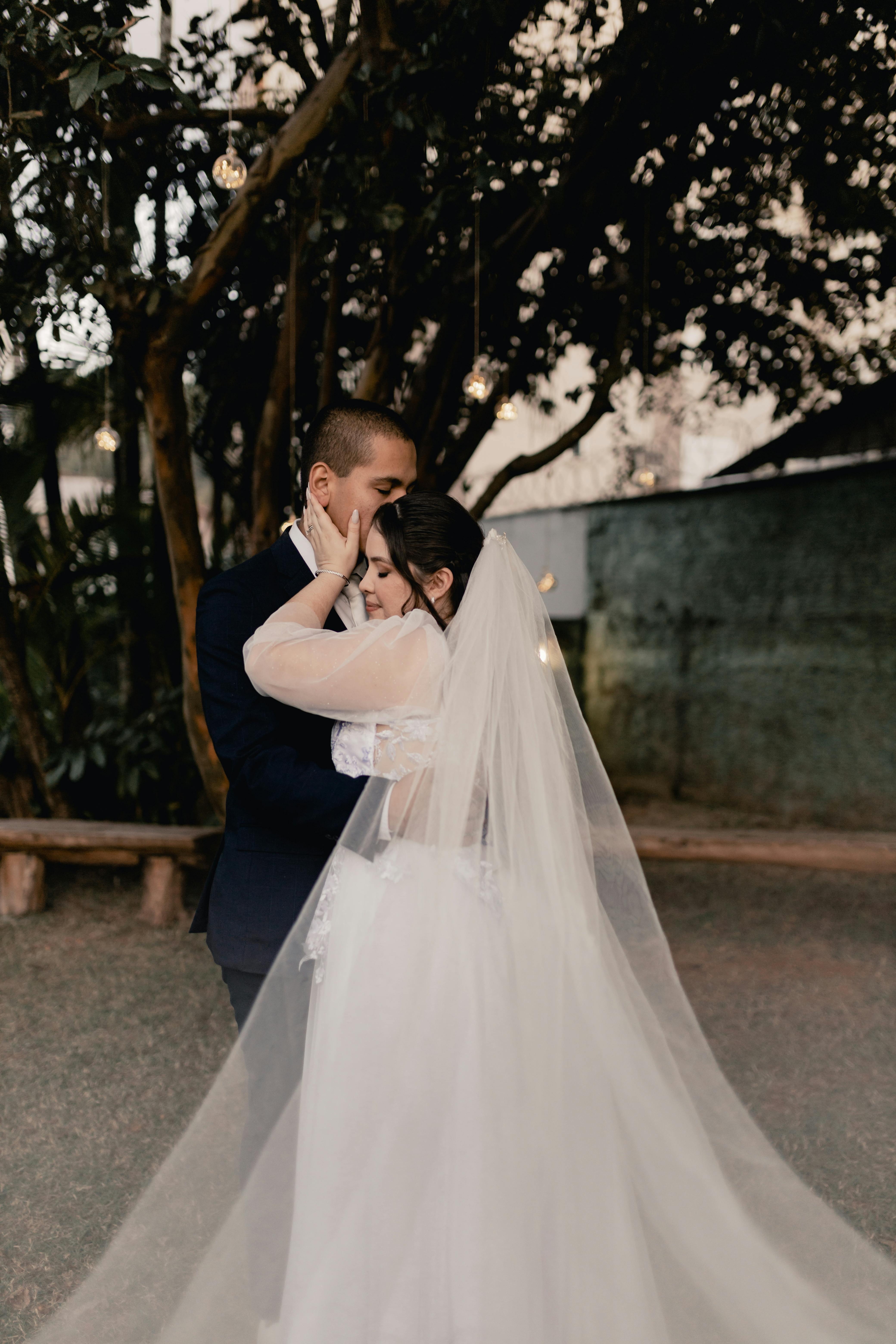 A bride and groom share an intimate moment outdoors under twinkling lights.