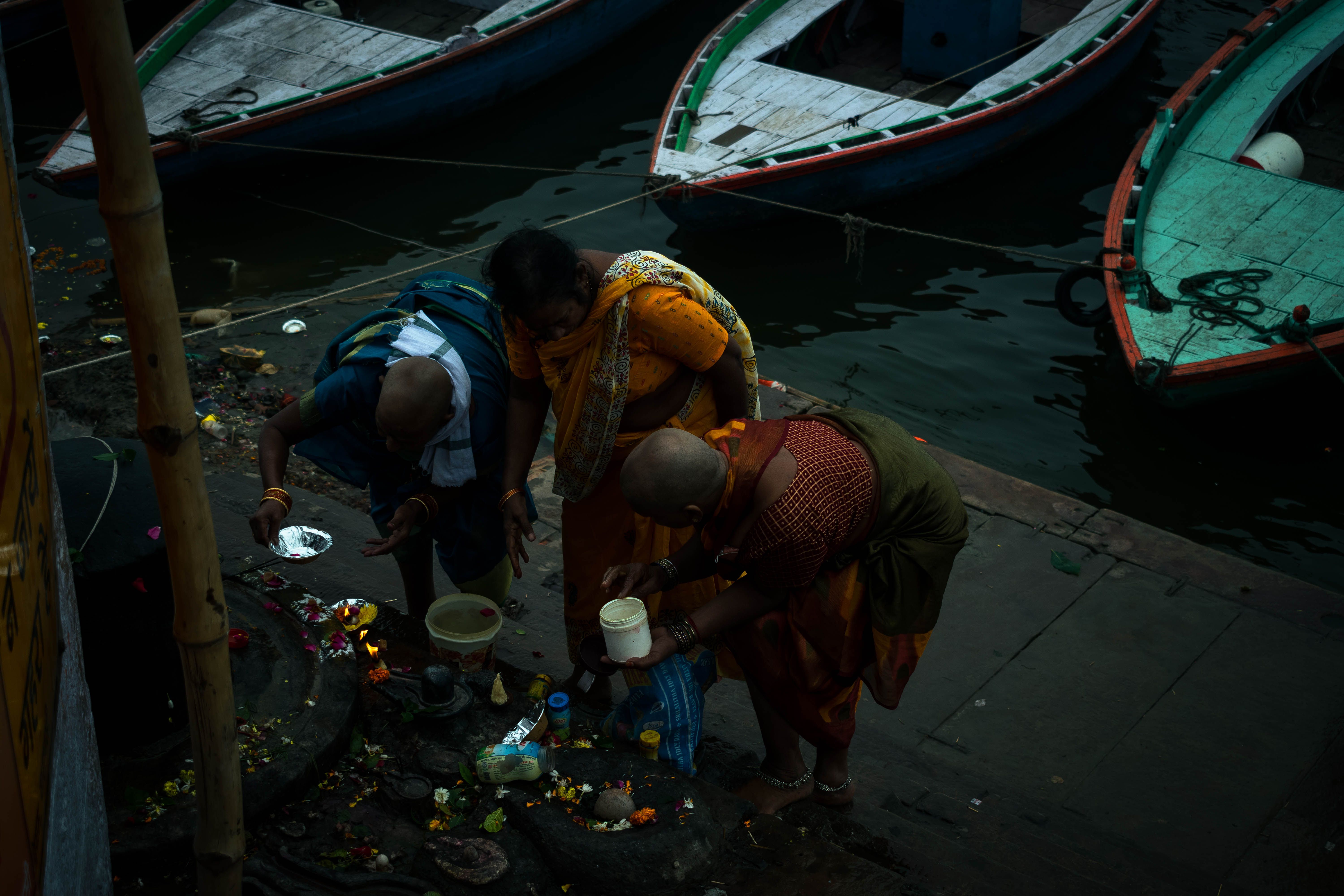 Three people make offerings of flowers, water and small lamps on riverside steps, a scene that echoes tarpan