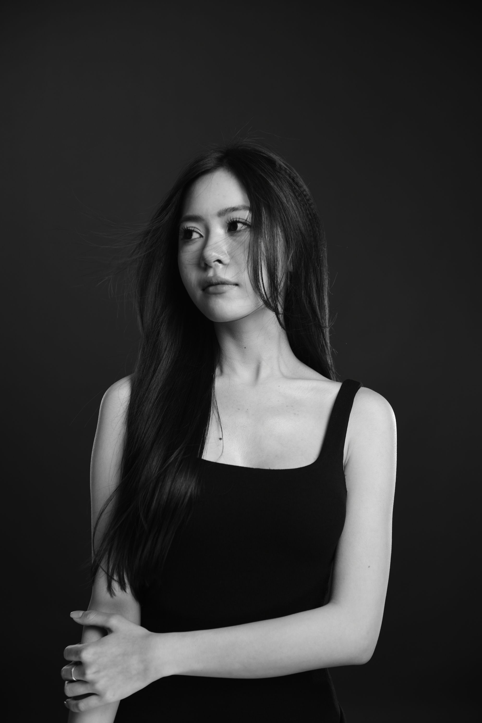 Stylish portrait of an Asian woman in a black tank top against a dark background.