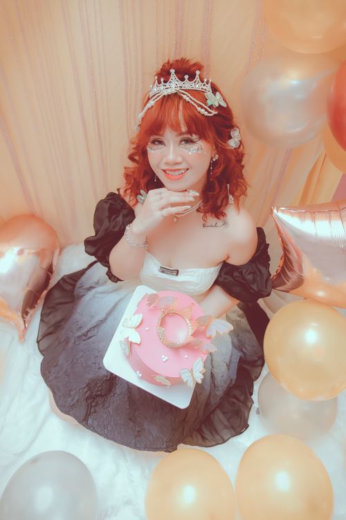 Free Smiling woman in crown celebrates birthday with a pink cake and colorful balloons. Stock Photo