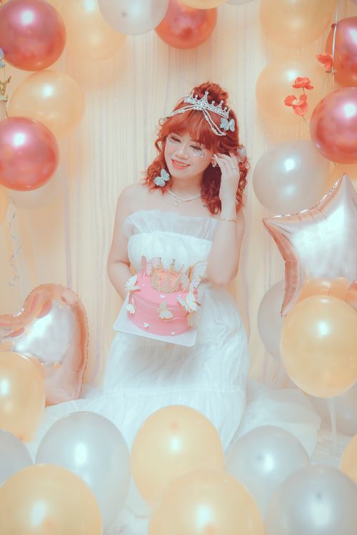 Free A happy bride with a bouquet sits among pastel balloons, wearing a tiara and a white wedding dress. Stock Photo