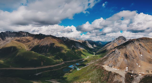 Stunning aerial view of a lush mountain valley with scenic roadways amidst dramatic skies.