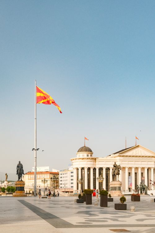 Free Panoramic view of Skopje highlighting neoclassical buildings and a national flag under a clear blue sky. Stock Photo