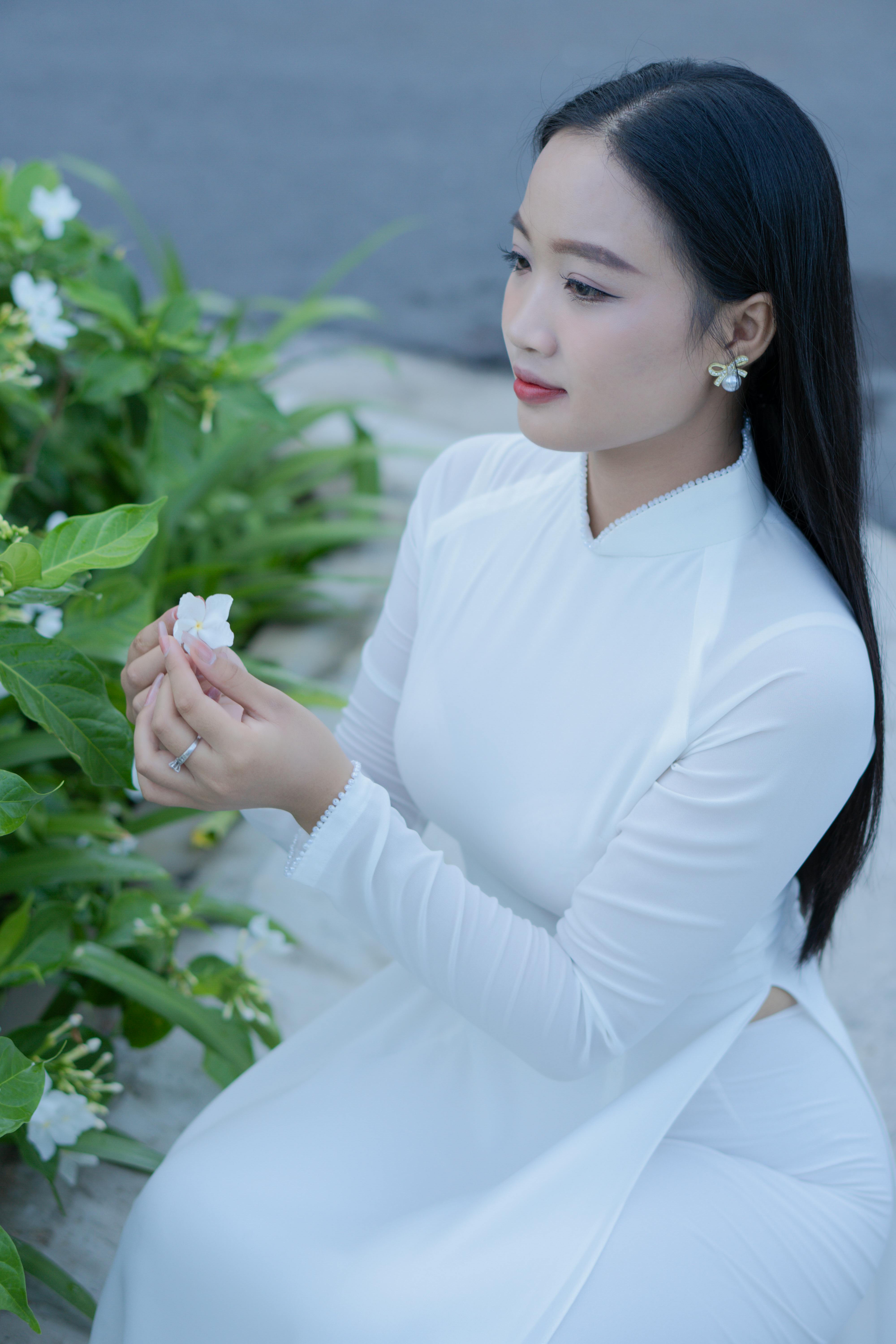 Young Vietnamese woman in a white ao dai, holding a flower with serene expression.