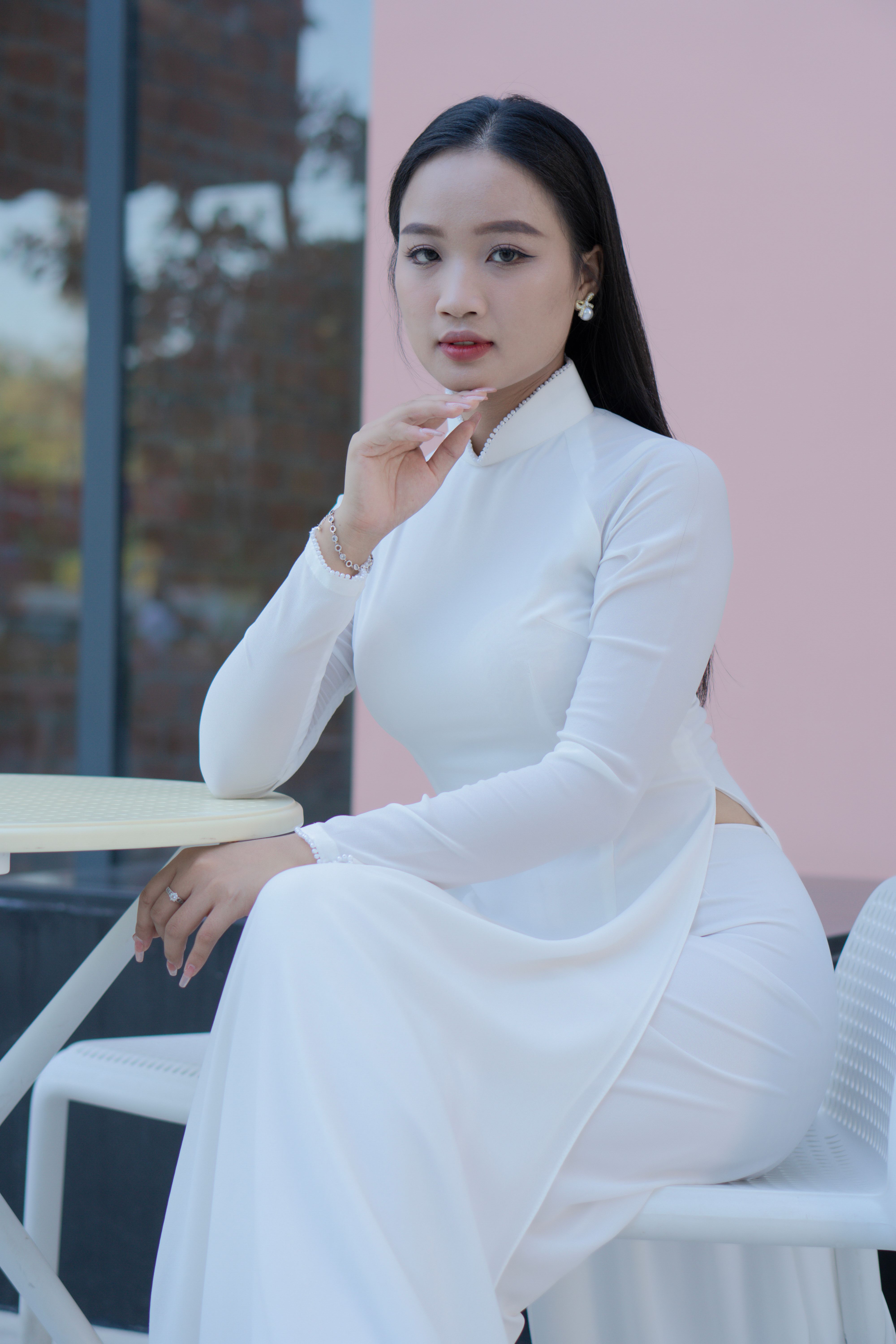 A serene Vietnamese woman in a white ao dai sitting elegantly at an outdoor café table.