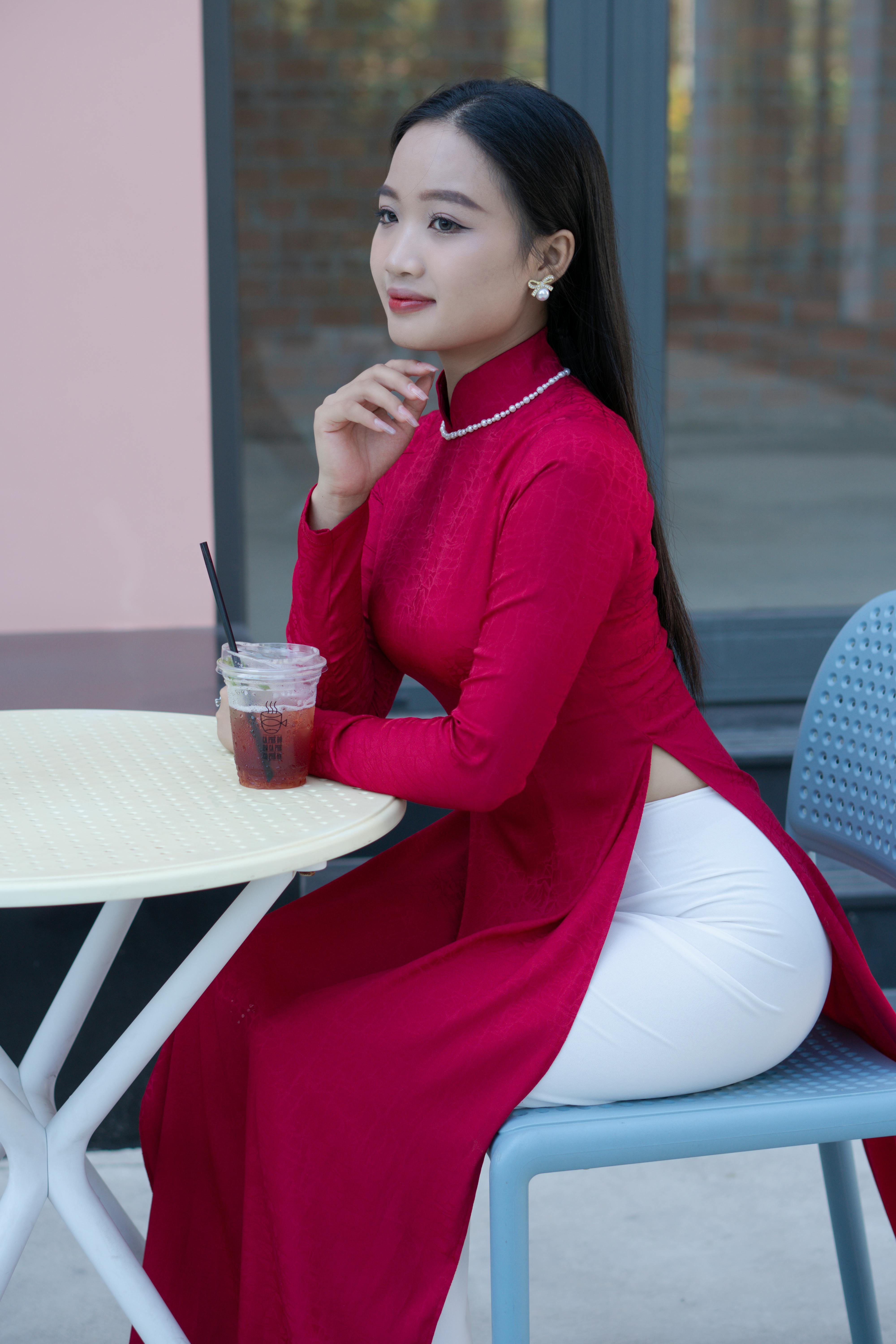 Asian woman in traditional ao dai sitting at a cafe table drinking, embodying elegance.