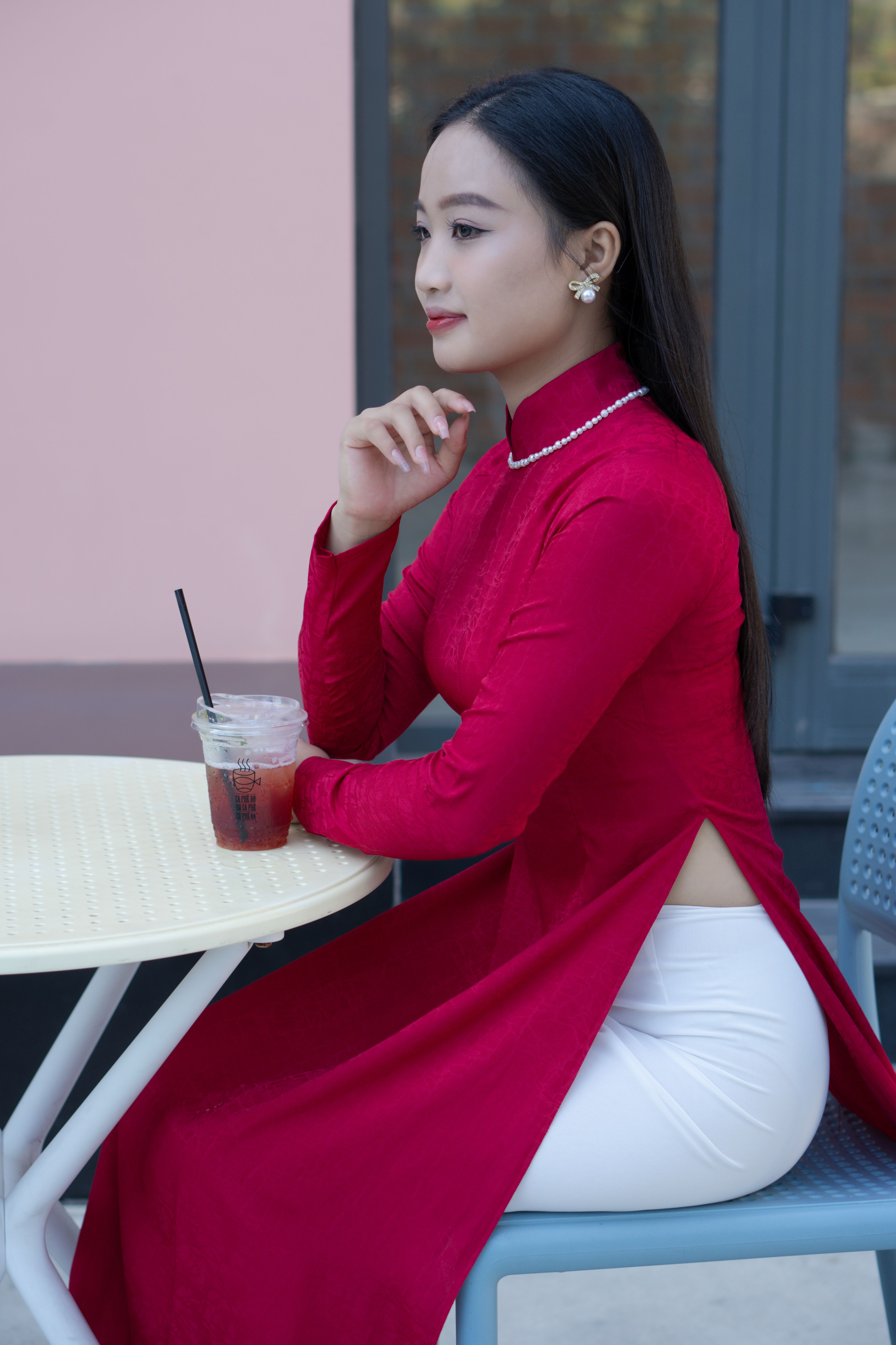 Portrait of a woman in a red ao dai, seated outdoors, exuding elegance and cultural charm.