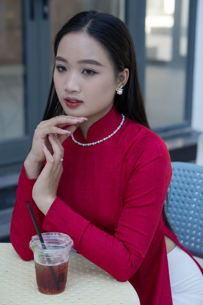 Portrait of a woman in traditional ao dai sitting at a cafe table with a drink.