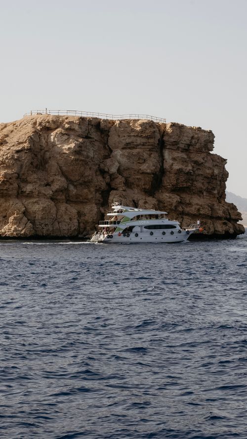 Free A luxury yacht sails by the rocky cliffs of Sharm El-Sheikh, Egypt, capturing a serene coastal view. Stock Photo