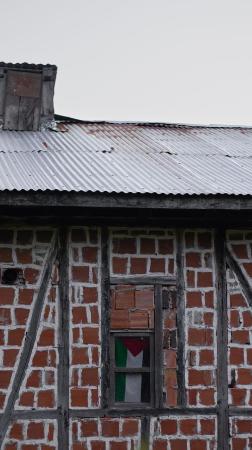 Free Brick wall building with Palestinian flag visible through window. Stock Photo