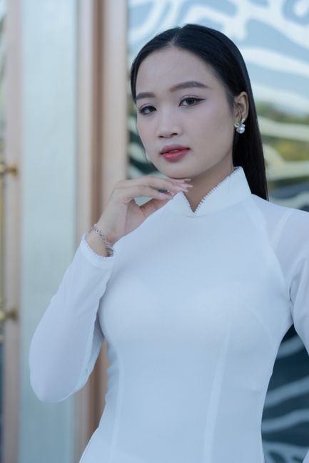 An elegant portrait of an Asian woman in traditional Ao Dai clothing, posing gracefully indoors.
