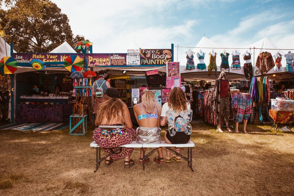 Bright festival scene featuring carnival booths and stylishly dressed women enjoying a sunny day.