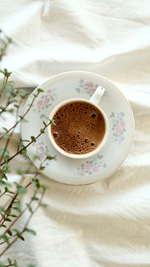 Free A top view of a floral patterned coffee cup on a white tablecloth, with a plant accent. Stock Photo