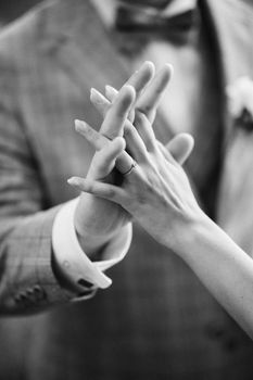 Monochrome wedding photo showcasing intertwined hands of a couple in formal attire.
