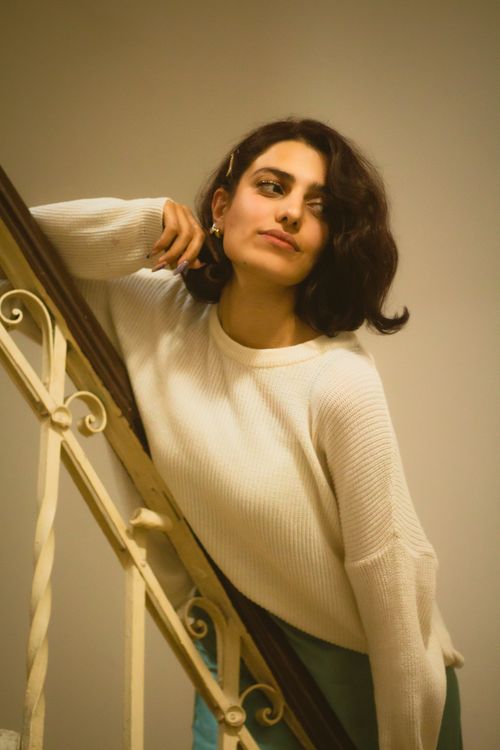 Free Stylish young woman in a white sweater posing on a staircase indoors. Stock Photo
