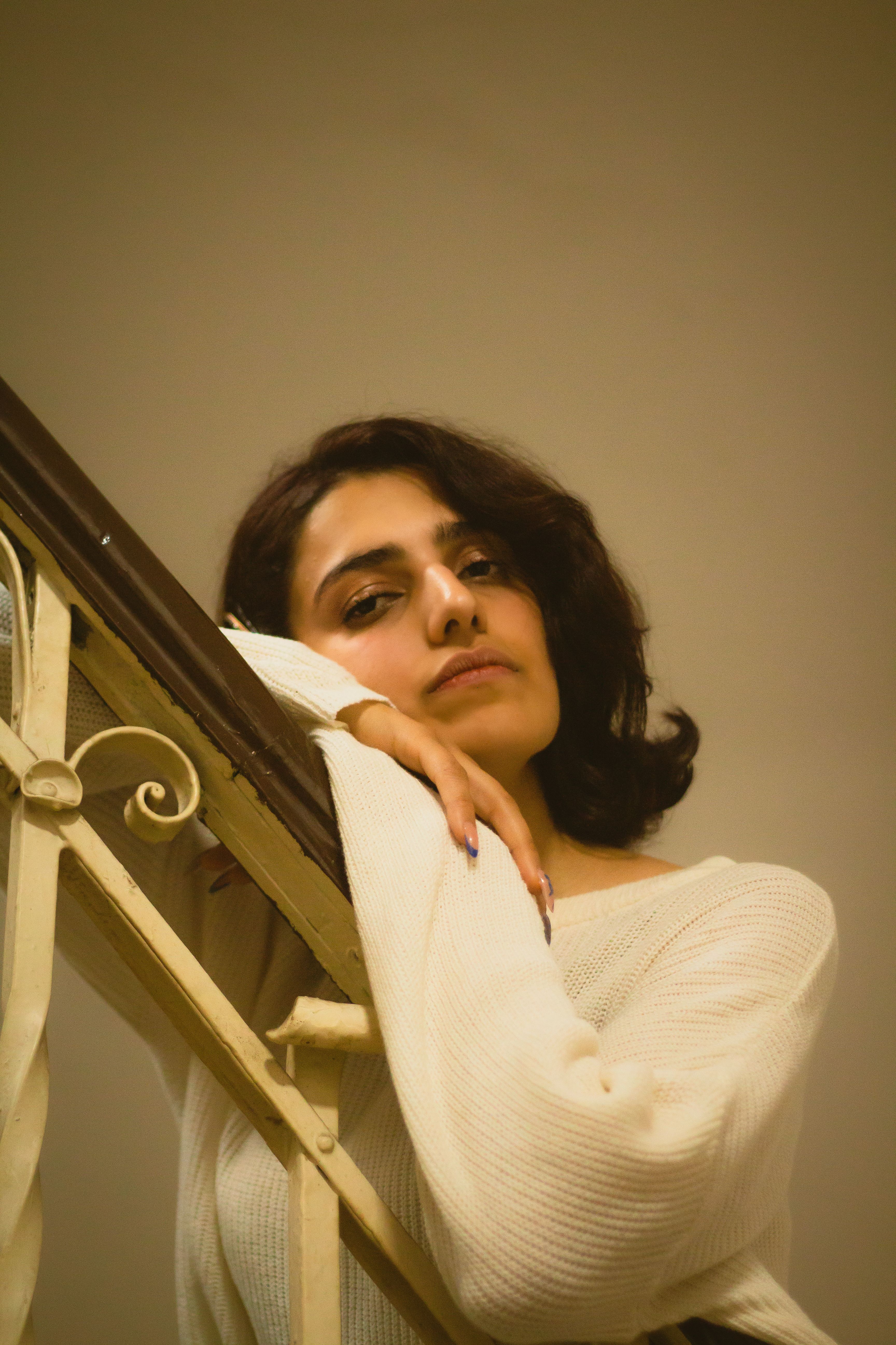 Woman in a cozy sweater leaning on a vintage stair railing indoors.