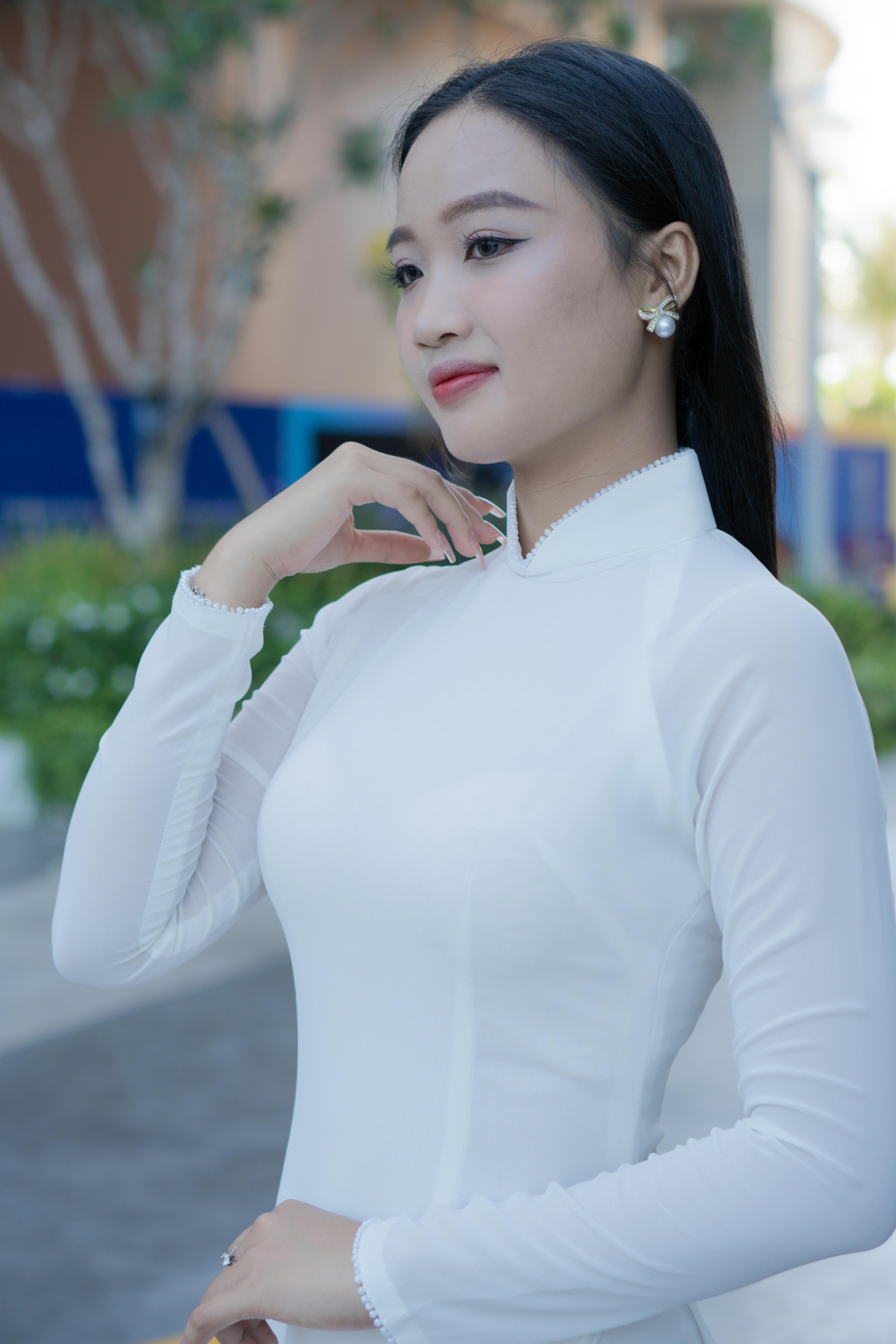 Portrait of an elegant Asian woman wearing a traditional white Ao Dai dress, outdoors.