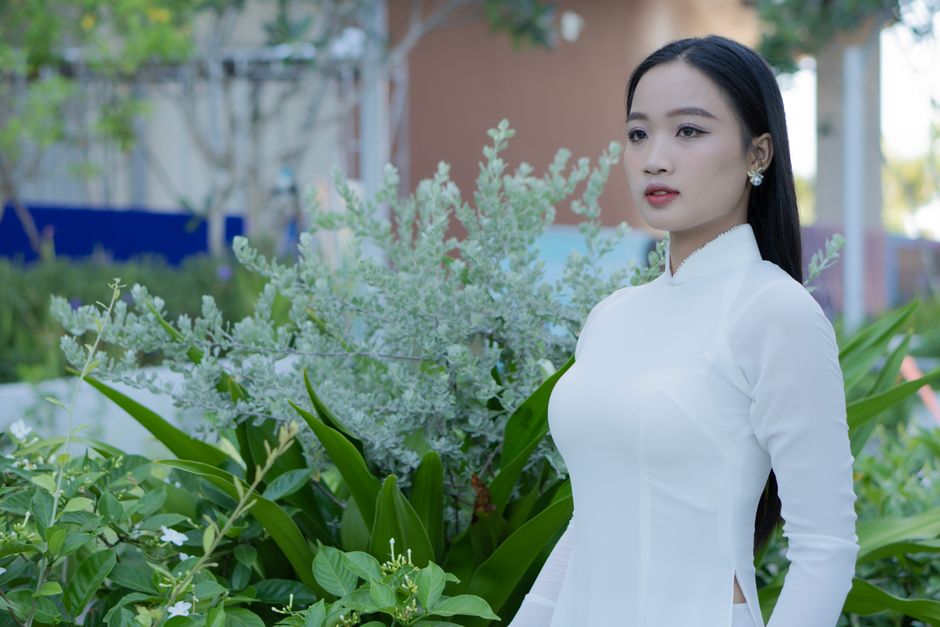 Portrait of a woman in traditional Vietnamese attire, surrounded by lush greenery.