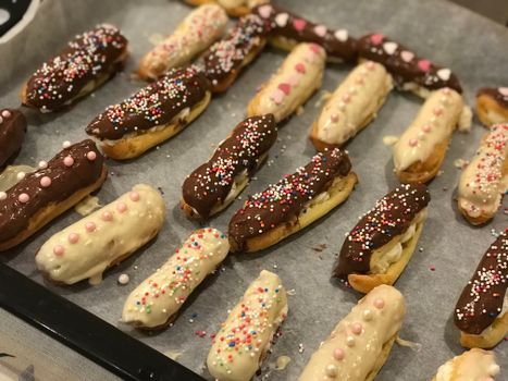 Colorful eclairs with chocolate and sprinkles on a baking tray.