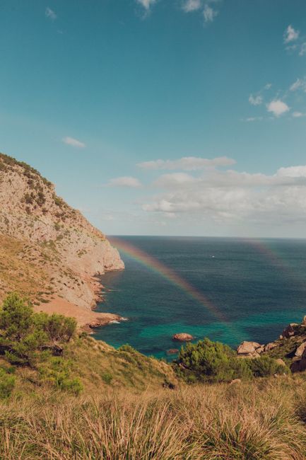 Explore the stunning Cales de Mallorca coastline with a vibrant double rainbow over the sea.
