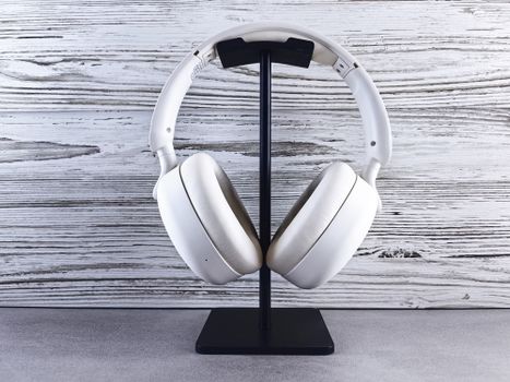 Stylish white wireless headphones displayed on a sleek stand against a wood background.