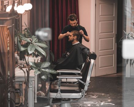 Barber styling a man's hair in a chic, modern salon interior, showcasing professional hairdressing skills.