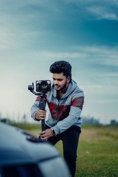 Young man operates a gimbal and camera setup outdoors for video recording.
