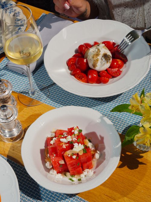 Free Top view of a restaurant table with burrata, watermelon salad, and white wine for a gourmet dining experience. Stock Photo