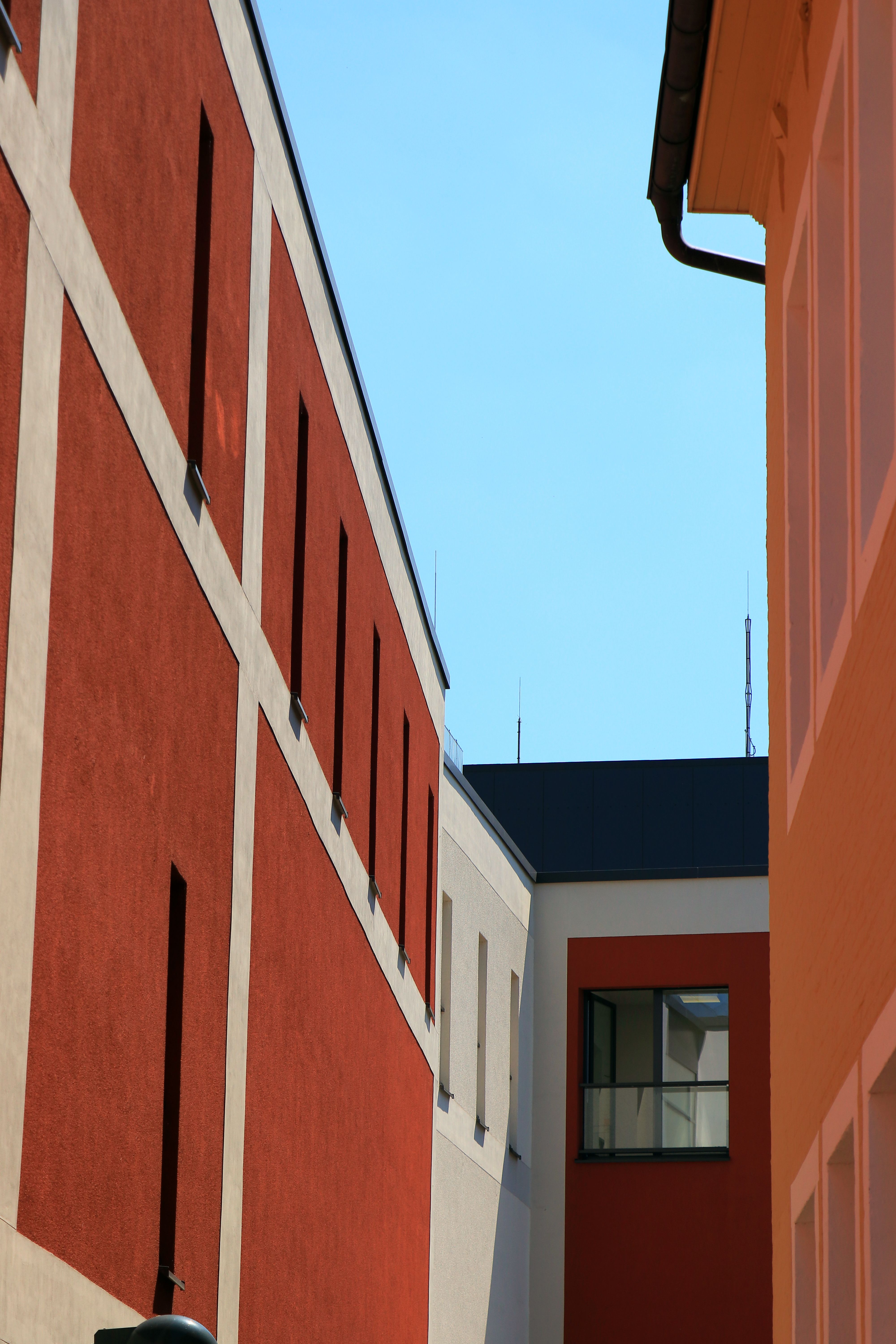 Free A vibrant urban alley with geometric patterns in orange, white, and red facades. Stock Photo
