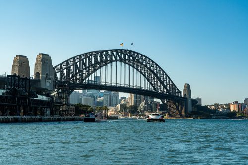 Free View of Sydney Harbour Bridge with city skyline and boats on a clear day. Stock Photo