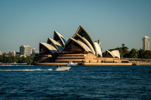Free Iconic Sydney Opera House surrounded by water and vibrant cityscape under clear skies. Stock Photo