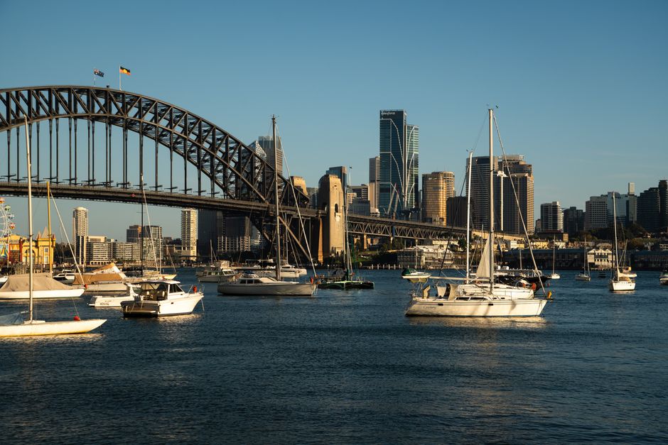 Scenic view of Sydney Harbour Bridge with boats and city skyline at sunset.