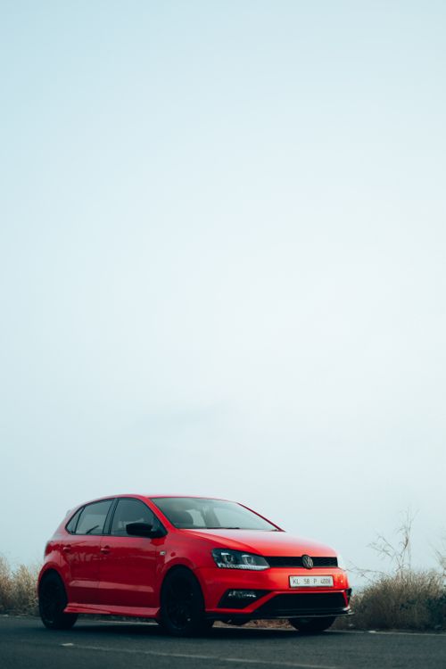 Free A vibrant red car parked on an open road against a clear blue sky, perfect for travel themes. Stock Photo